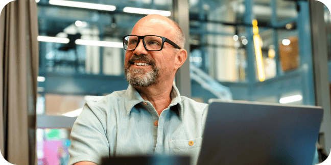 Smiling man with glasses and a beard sitting in front of a laptop.