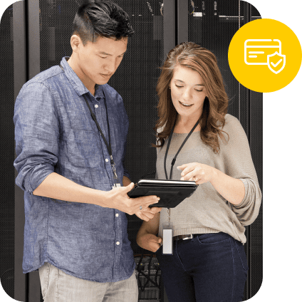 Two IT professionals looking at a tablet in a server room with a secure payment icon.
