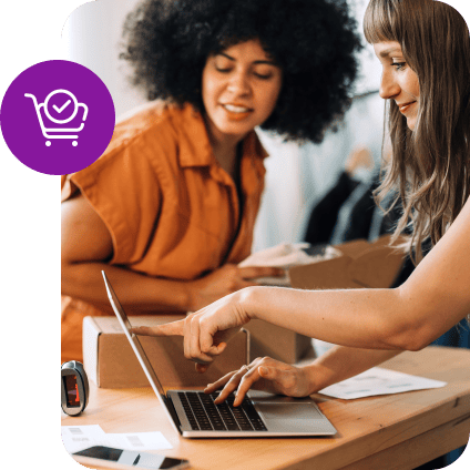 Two women managing e-commerce orders on a laptop with a purple shopping cart icon.