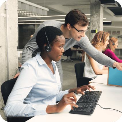 Two colleagues collaborating at a desktop computer in an open-plan office.