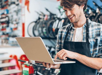 Bike shop employee smiling while holding and typing on a laptop computer.
