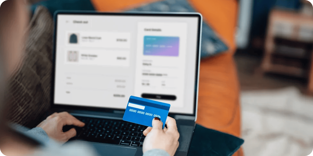 Person holding a blue credit card while making an online purchase on a laptop.