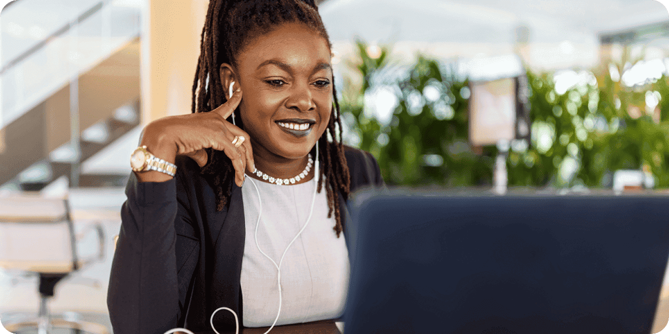 Professional woman with locs smiling at her laptop screen in a modern office.