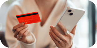 Une personne tenant une carte de crédit rouge et un smartphone blanc pour effectuer un paiement en ligne.
