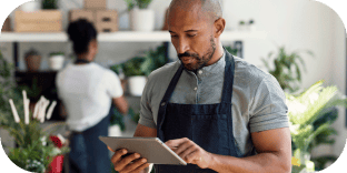 Un homme portant un tablier utilise une tablette numérique dans une jardinerie ou une boutique de fleurs.