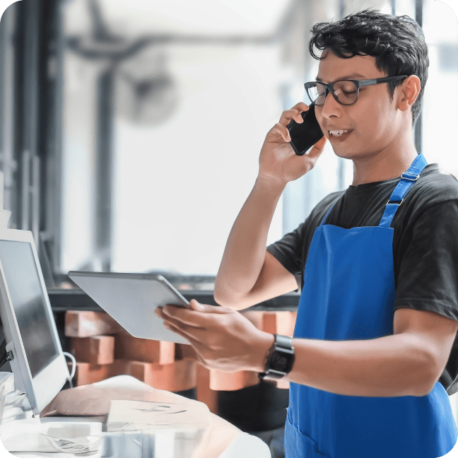 Service worker wearing glasses talking on a smartphone while checking a tablet.