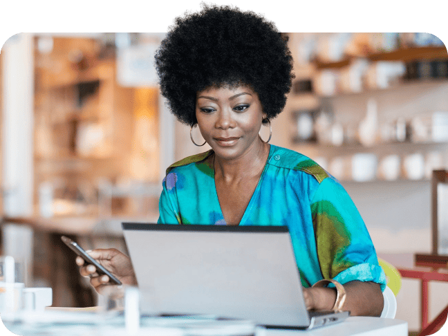 Professional woman looking at her laptop screen while holding a smartphone.