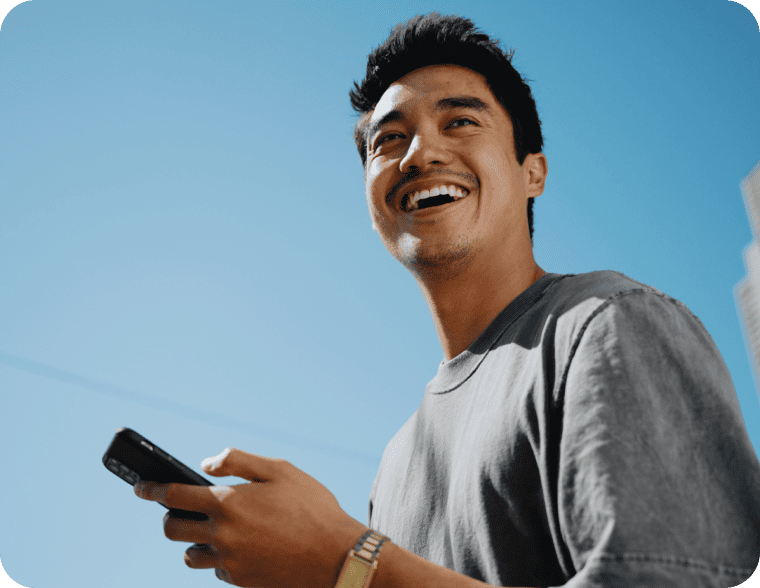 Happy young man holding a phone outdoors under a bright blue sky.