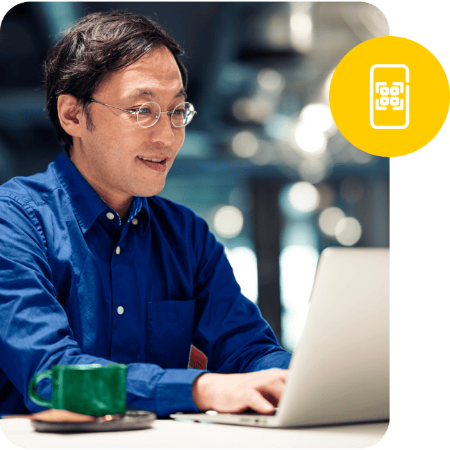 Man wearing glasses working on a laptop with a yellow QR code badge overlay.