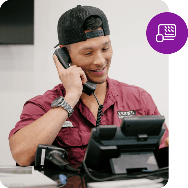 Man wearing a cap talking on a desk phone with a purple payment card icon overlay.