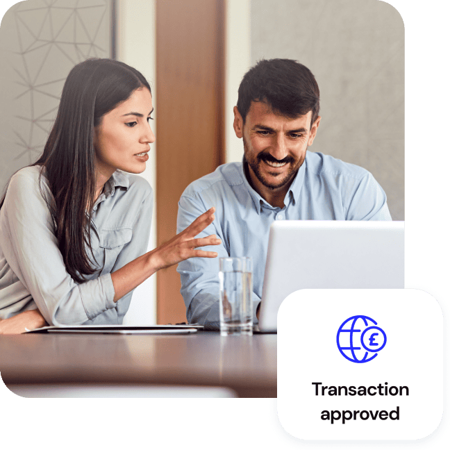 A woman explaining something to a colleague at a laptop with a Transaction approved badge.