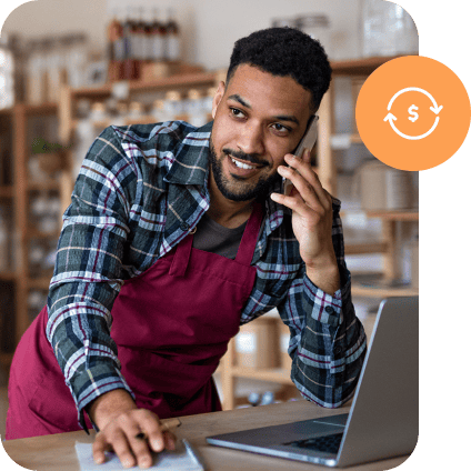 A small business owner managing orders on a laptop while assisting a customer over the phone