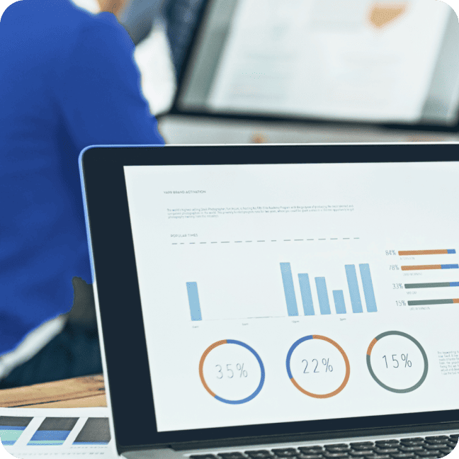 A laptop screen displaying a business data dashboard with blue bar charts and circular infographics.