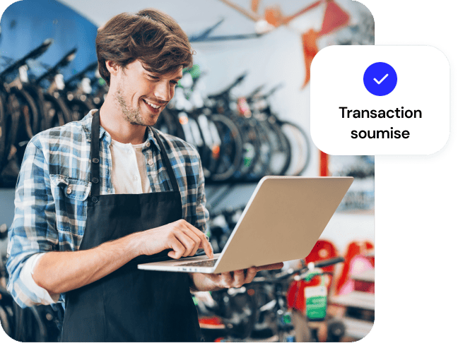 Un commerçant enregistre une vente sur un ordinateur portable. Superposition : Transaction soumise.