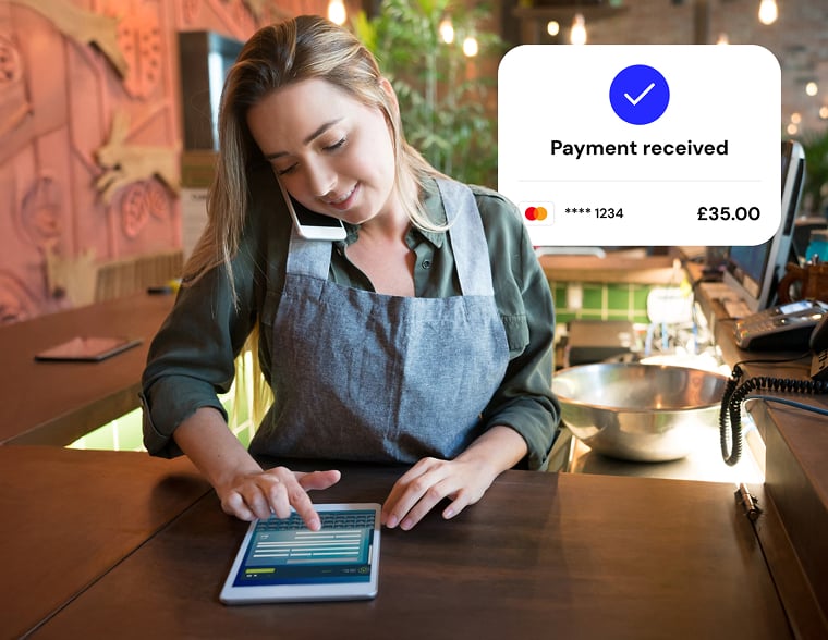 A person speaking on a mobile phone while using a tablet with a “Payment received” confirmation.