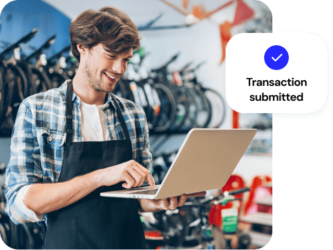 A shop owner processes a sale on a laptop. Overlay: Transaction submitted.