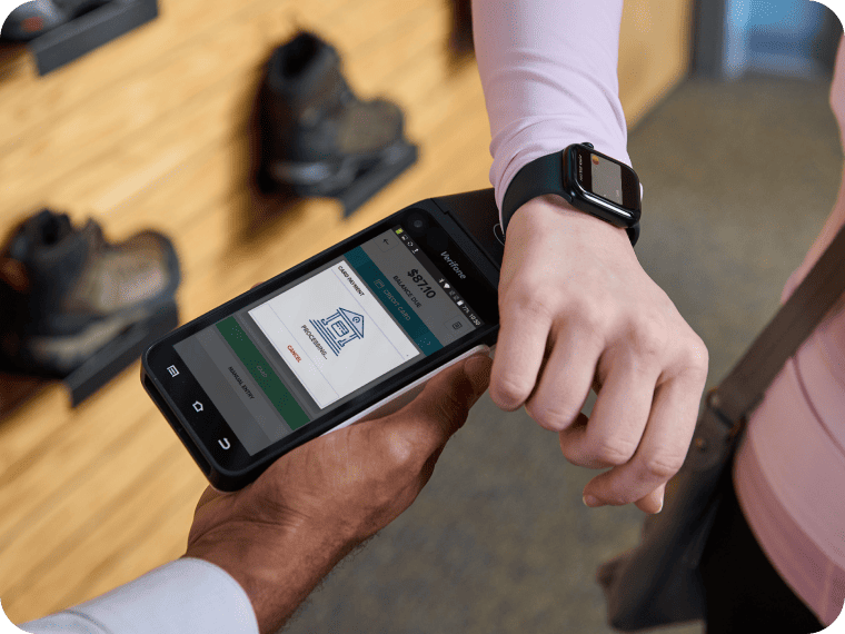 Closeup of a person wearing a smartwatch taping a handheld payment terminal to pay