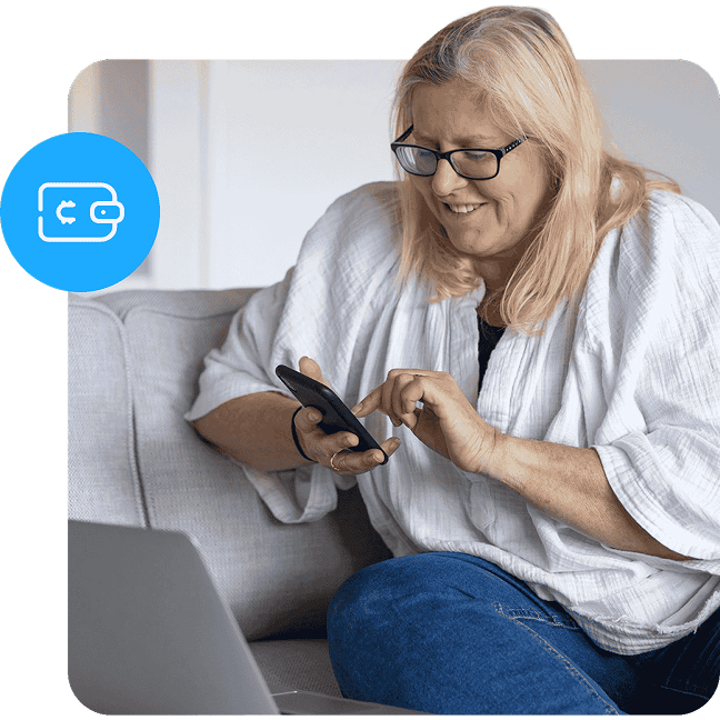 A woman with blonde hair and glasses smiles while using a smartphone on a couch.