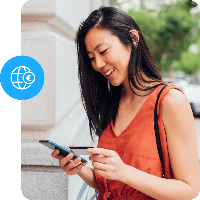 Smiling woman holding a credit card and phone with a global currency icon overlay.