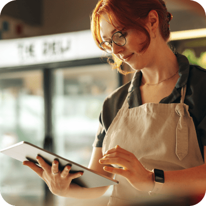 A woman with glasses and an apron using a digital tablet in a store.