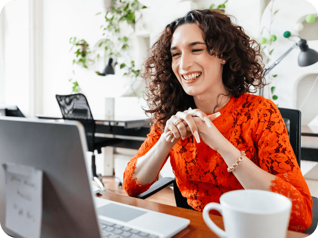 Happy professional with curly hair smiling during a video call on a laptop at work.