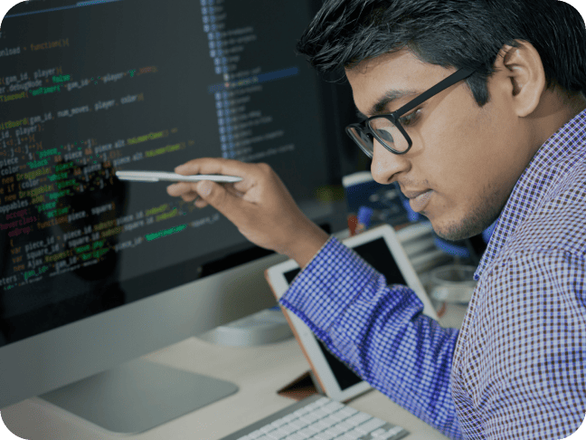 Un homme portant des lunettes pointe un stylet vers l'écran d'un ordinateur de bureau affichant du code.