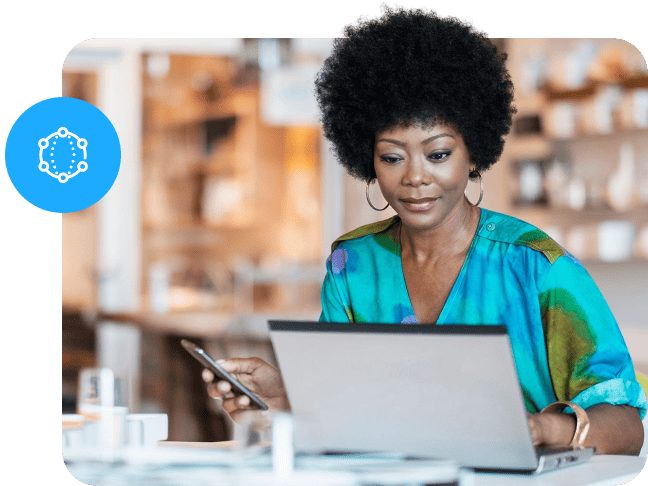 A woman working on a laptop while holding a phone next to a blue network icon overlay.