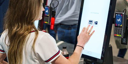 A woman using a touchscreen self-checkout kiosk with Atlanta Braves card readers nearby.