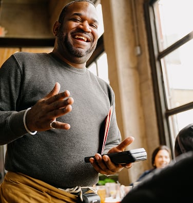 Smiling server holding a handheld POS payment terminal while talking to customers.