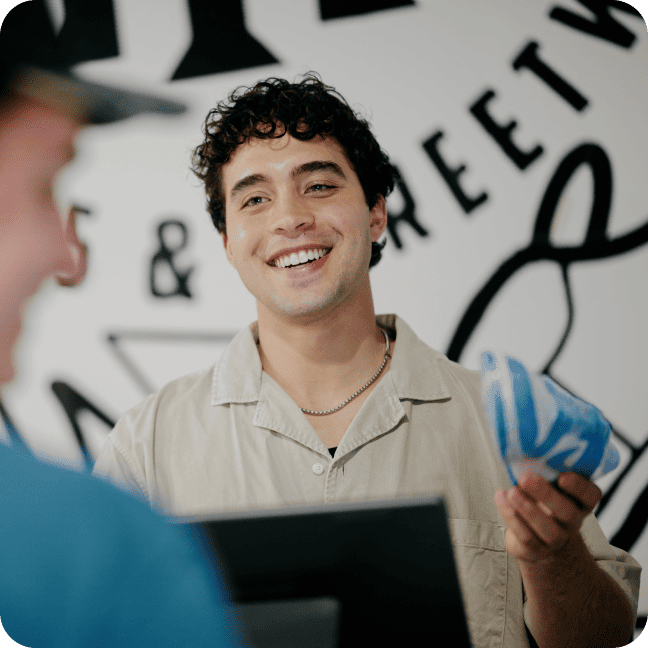Smiling cashier holding merchandise while interacting with a customer at a checkout.