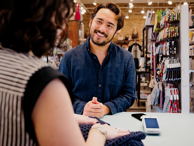 Man smiling at a retail store counter while making payment to female cashier
