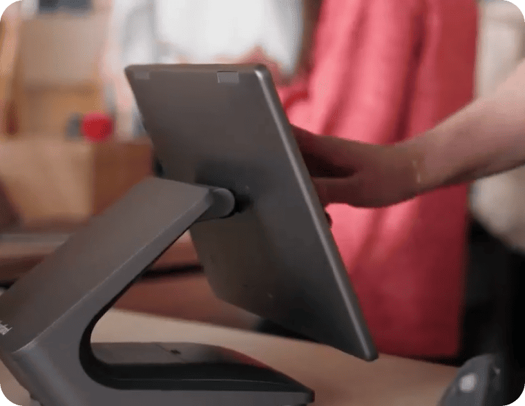 A hand reaching out to touch the screen of a modern desktop POS tablet stand.