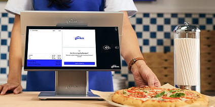 Hand holding a mobile restaurant POS terminal over a table with food and drinks.