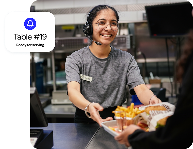 A quick service restaurant employee smiling while handing out an order to a customer.