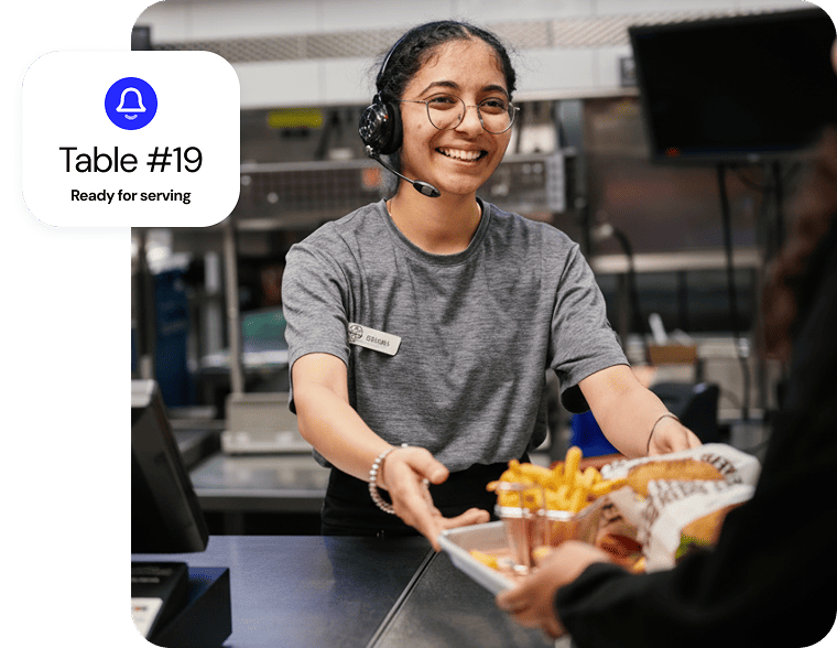 A quick service restaurant employee smiling while handing out an order to a customer.