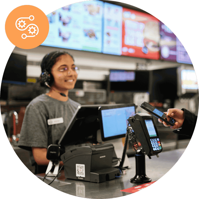 An employee wearing a headset greets customers at a quick-service restaurant point of sale system.