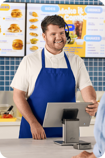 A QSR staff member wearing an apron takes a customer’s order at a countertop POS.