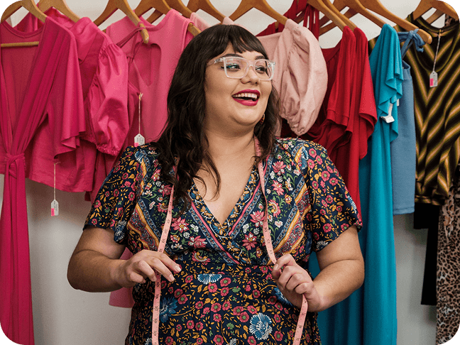 Retail worker stands in front of a rack of colorful clothing while holding a measuring tape.