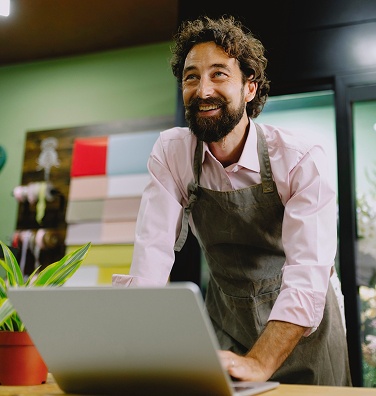 Retail employee working on a laptop at a shop counter.