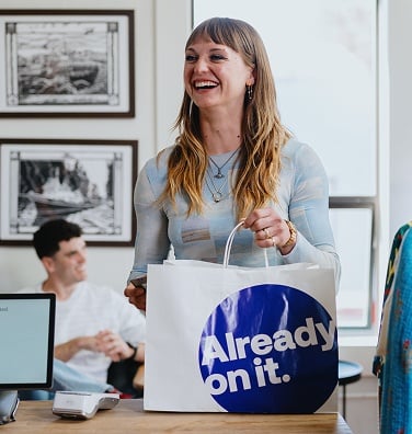 Smiling customer holding a Global Payments shopping bag at a checkout counter.