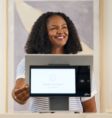 A smiling retail worker using a Genius countertop device.