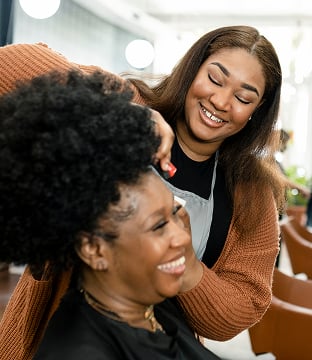 A smiling hairdresser styles a client’s hair in a bright salon.