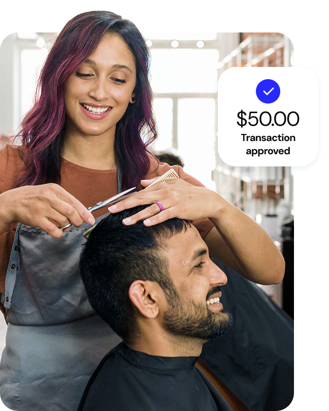 A smiling hairstylist cuts a client’s hair with a UI callout overlay that says “$50.00, transaction approved.”