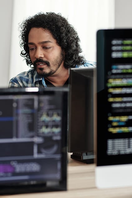 Male software engineer analyzing code on desktop screens at work.