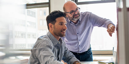 Two male professionals collaborating on a project in front of a monitor.