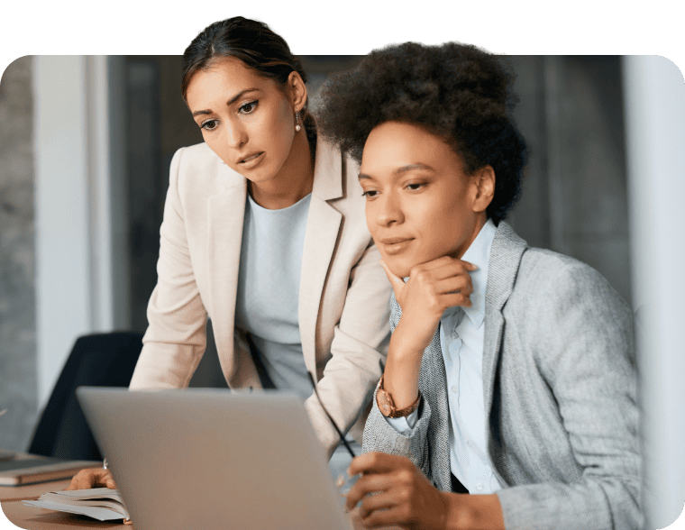 Two businesswomen focused on a laptop screen during a meeting.