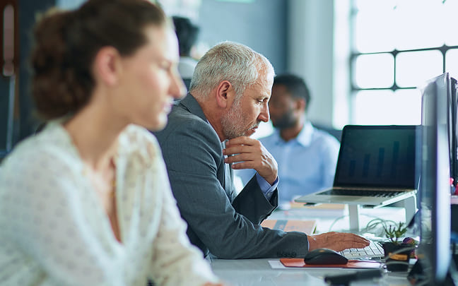 Senior businessman sitting at a desk and focused on his computer screen.