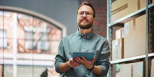 A man smiles and holds a tablet while standing in a warehouse.
