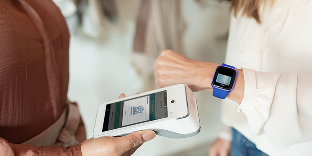 A woman holds her smart watch close to a payment terminal to complete her payment.