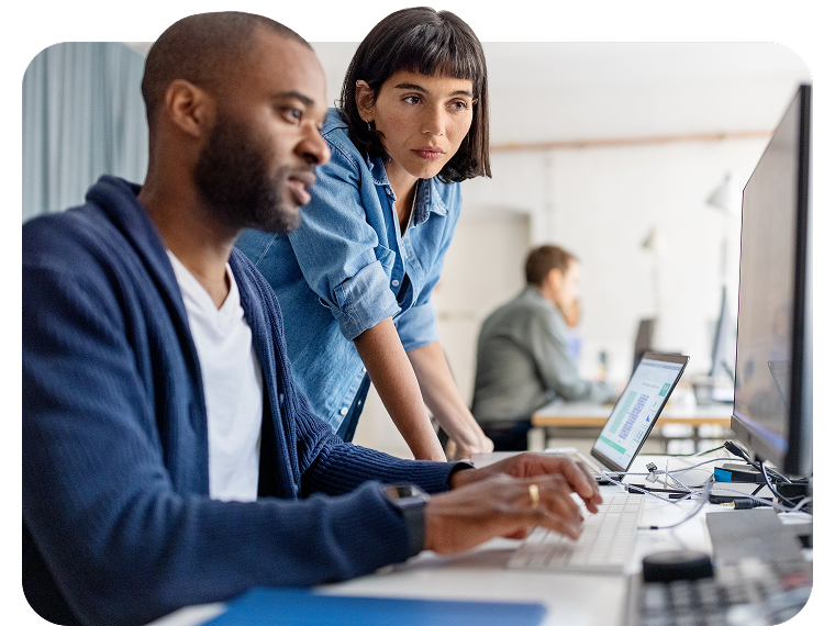 A man and a woman in an office setting look at a computer screen together.